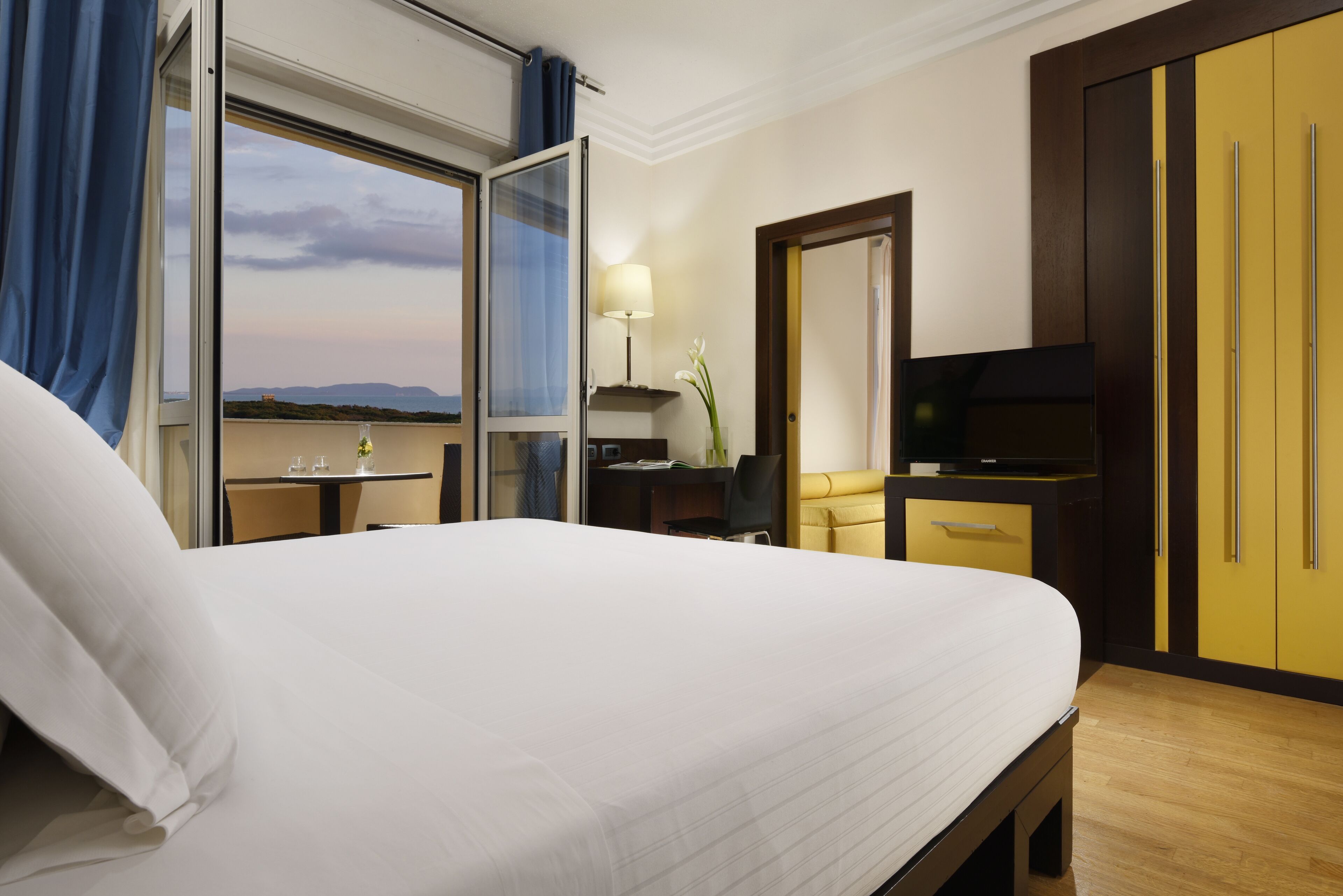 A hotel room with a large bed, a desk with a chair, a television, and a wardrobe.