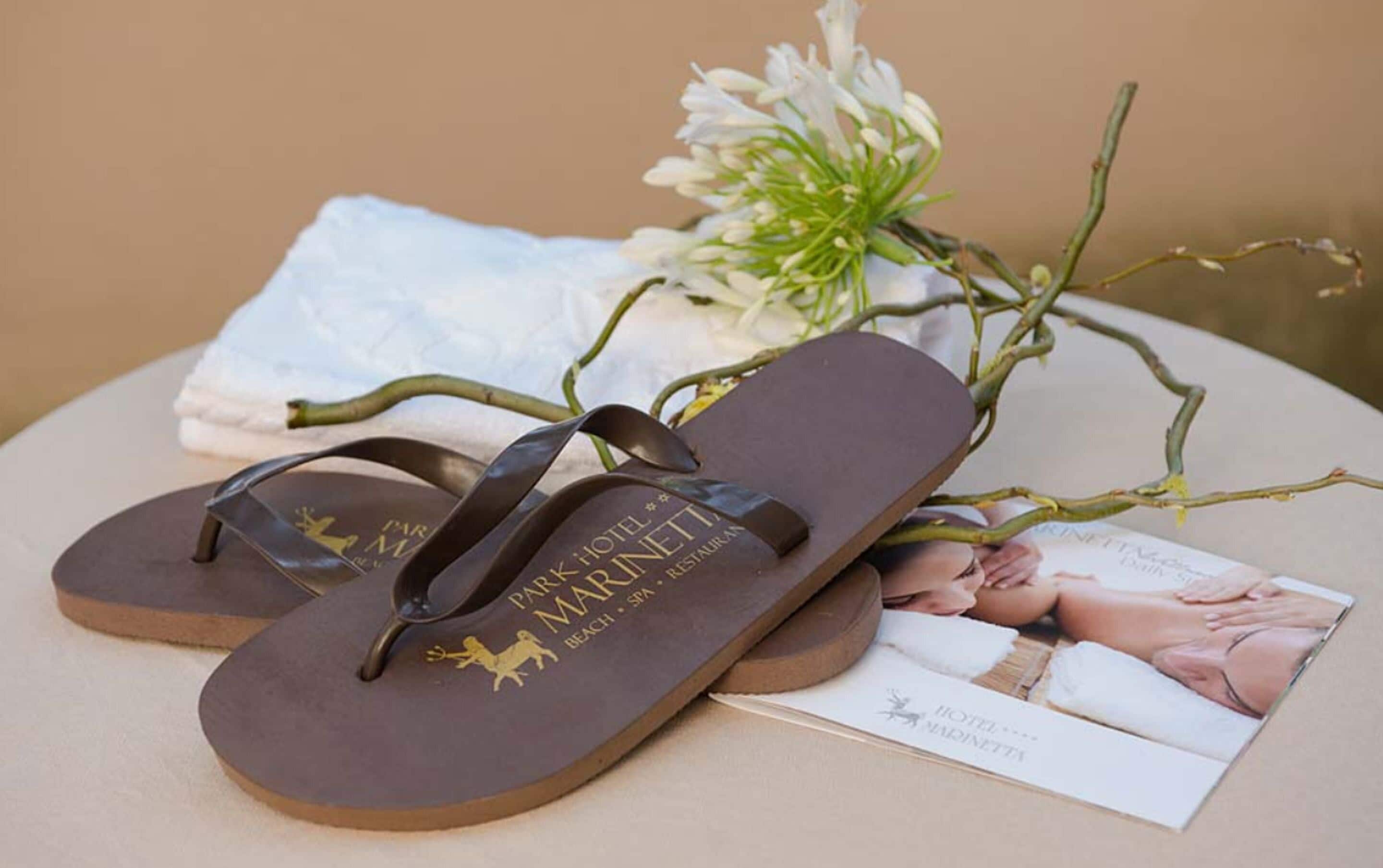 A pair of flip-flops with a logo, a white towel, and a magazine on a round table.