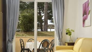 Quarto com um sofá amarelo, uma mesa de jantar com cadeiras e vista para árvores e uma cerca através de uma porta de vidro.