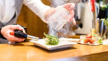 Una persona preparando un plato con un utensilio humeante, un plato y un cuenco pequeño de ingredientes sobre una mesa de madera.