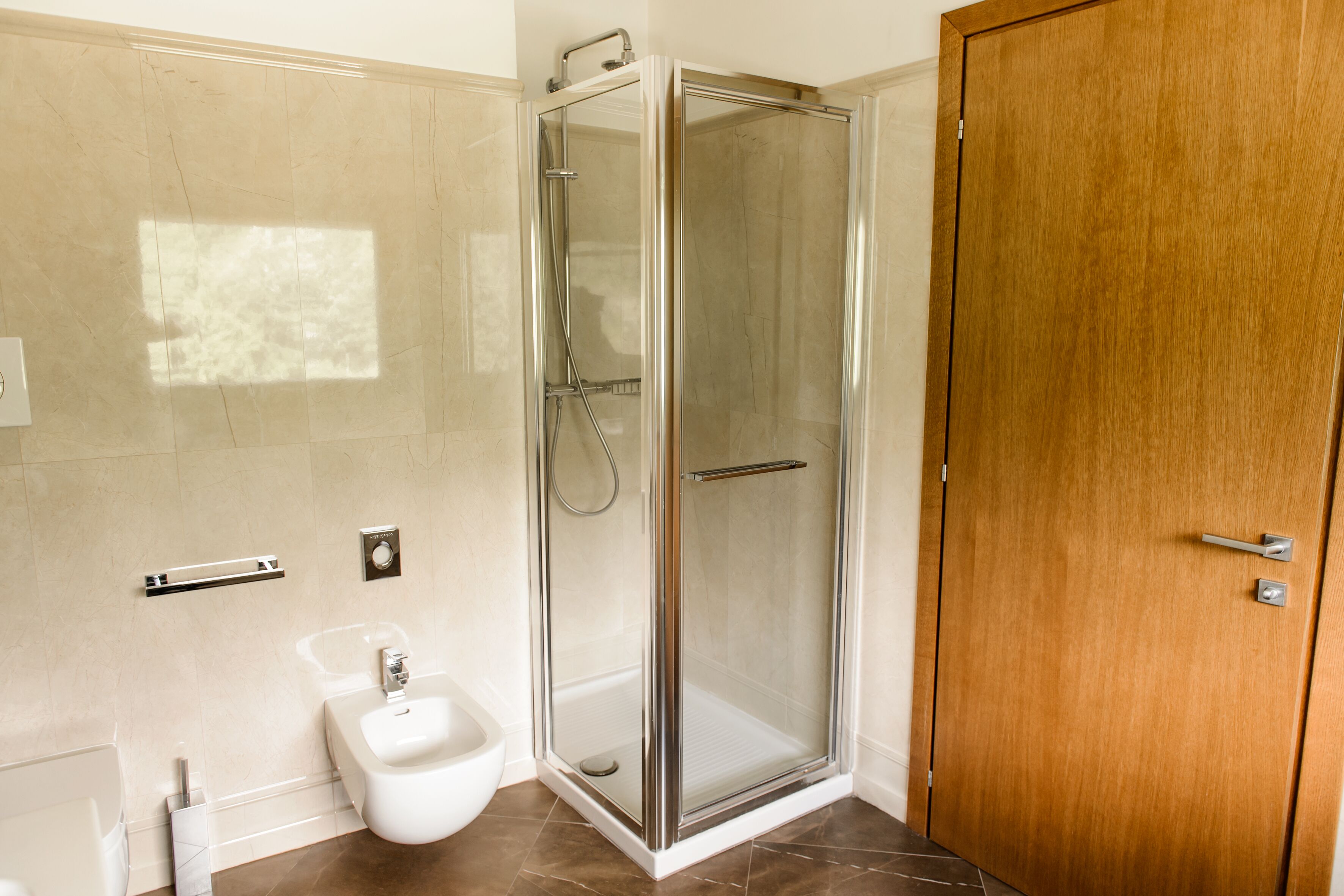 A modern bathroom with a glass-enclosed shower, a bidet, and a wooden door.
