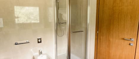 Un baño moderno con ducha de vidrio, un bidé y una puerta de madera.