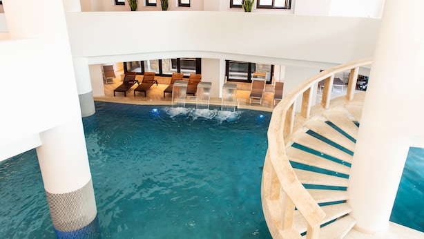 Una piscina interior de varios niveles con escalera, zona de descanso y grandes ventanales.