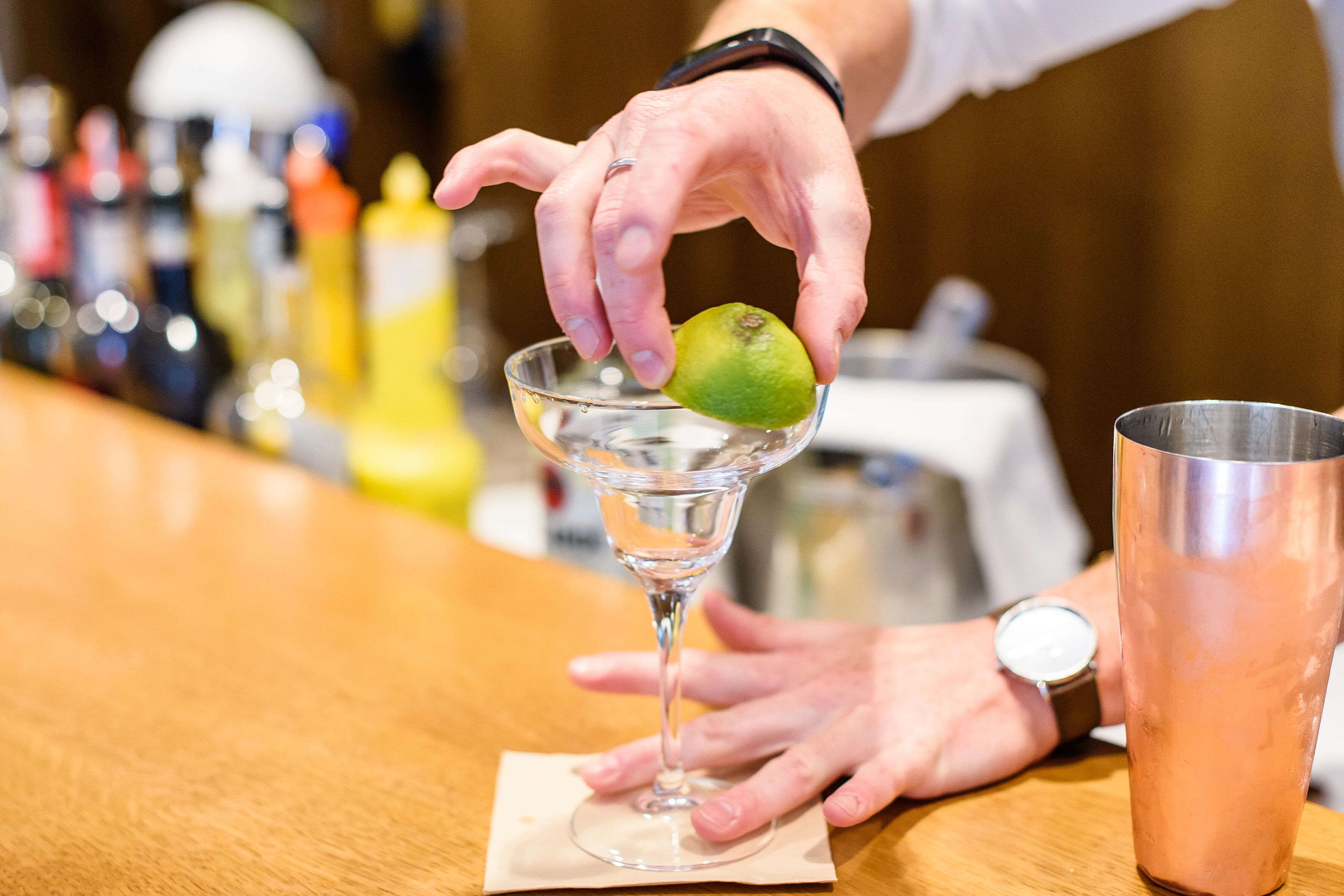 Een bartender bereidt een drankje toe met een limoen in een martini-glas.