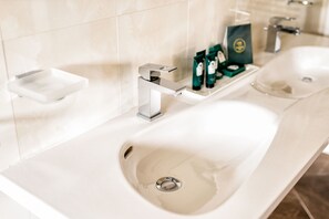 Un baño moderno con un lavamanos blanco, un espejo y un estante con artículos de aseo.