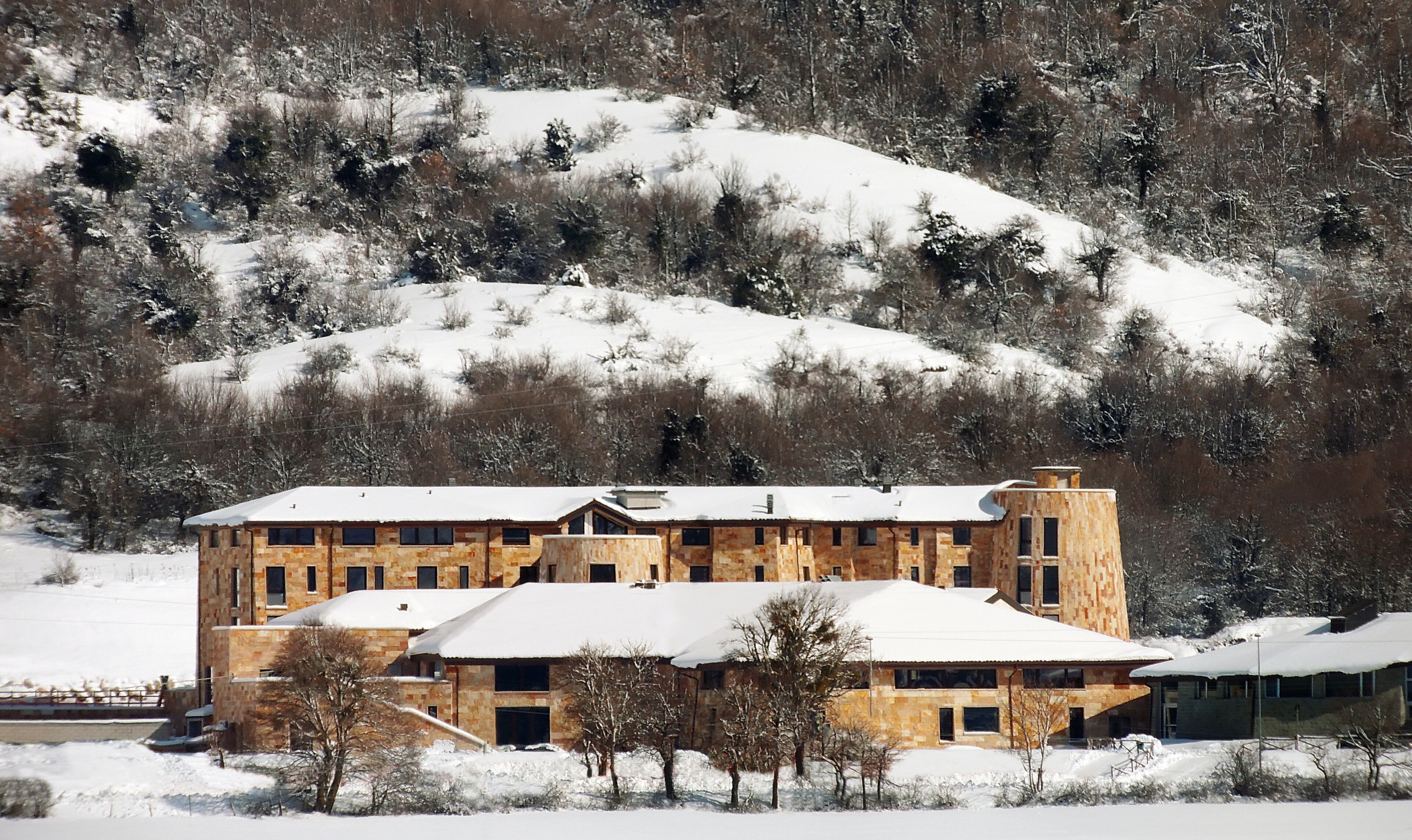 A multi-story stone building with a snow-covered roof, surrounded by a snowy landscape and trees.