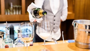 Un bar con una persona sirviendo una bebida en un vaso, una botella de champán y un cubo de hielo.