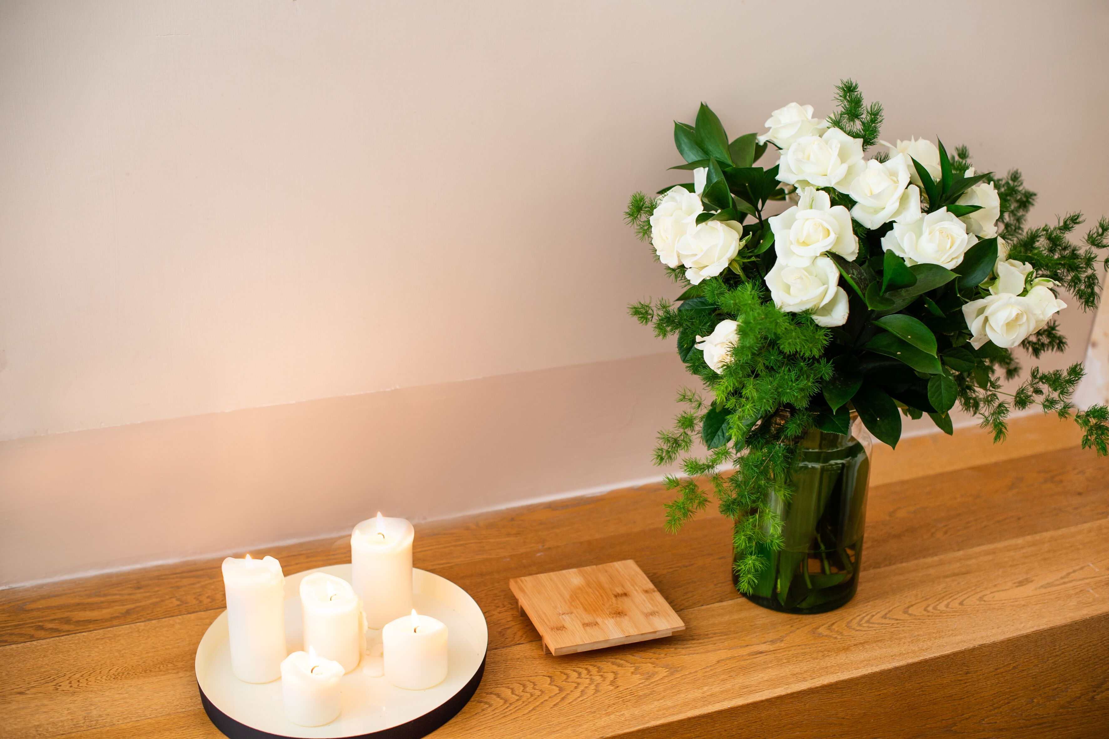 A wooden table with a vase of white flowers and several lit candles.