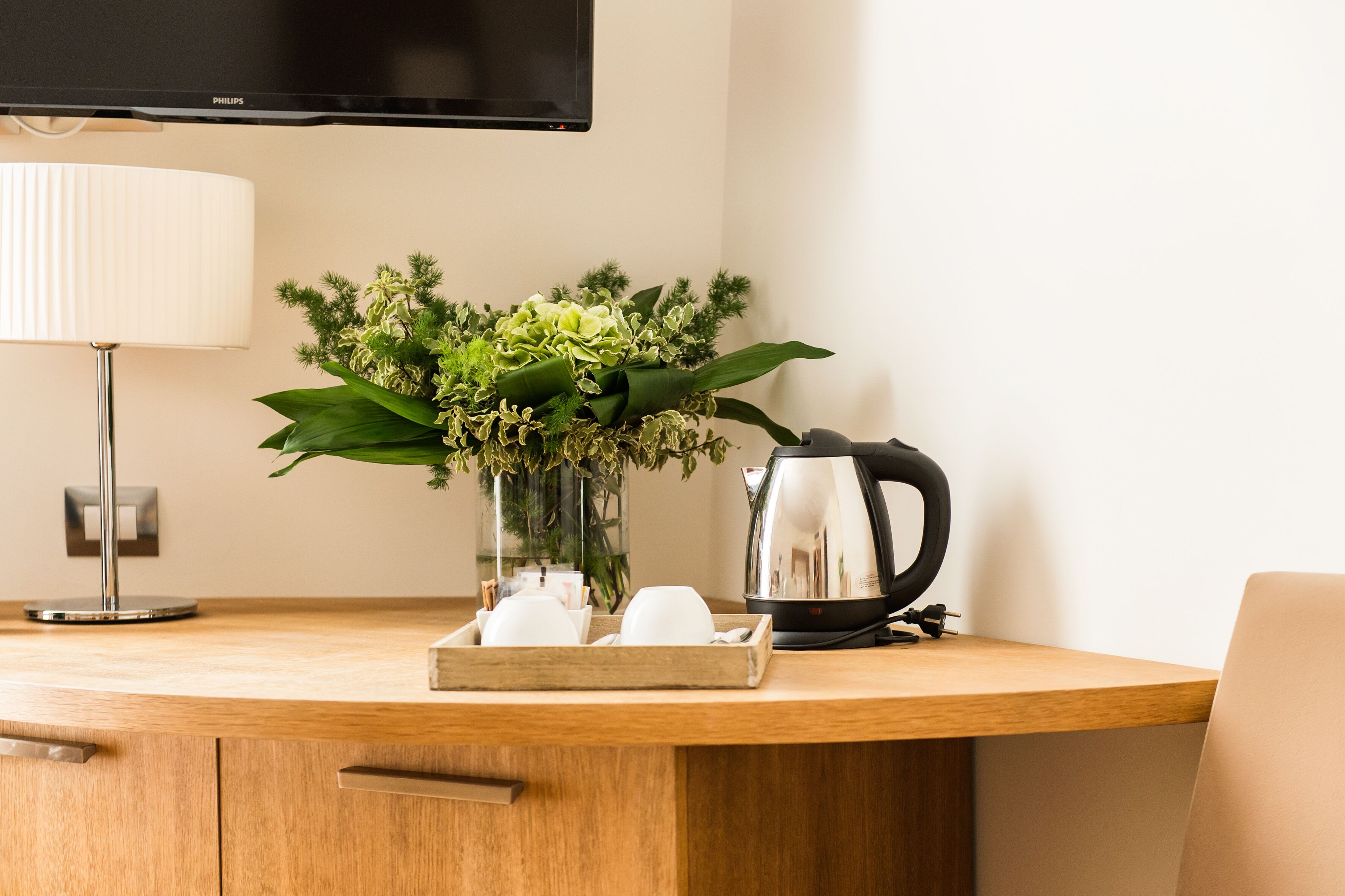 Ein Holztisch mit einer weißen Lampe, einer Pflanzvase mit Grünpflanzen, einer Ablage mit weißen Tassen und einer schwarzen Kaffeemaschine.
