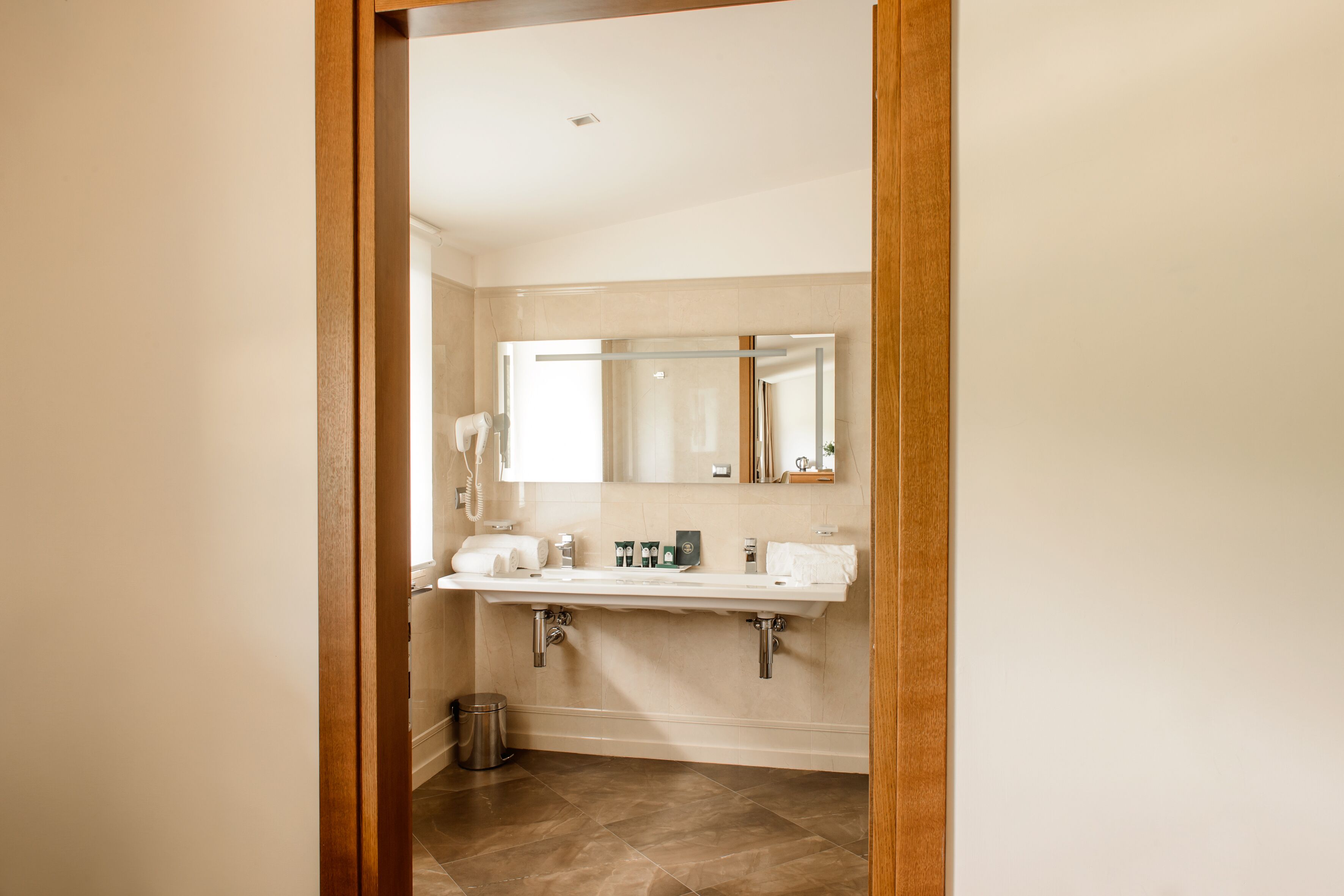 Un bagno con due lavandini, uno specchio e un cestino.