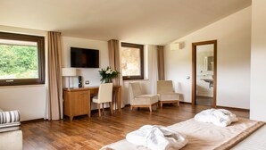 Habitación de hotel con cama, dos sillas, escritorio, televisor y baño visible a través de una puerta abierta.