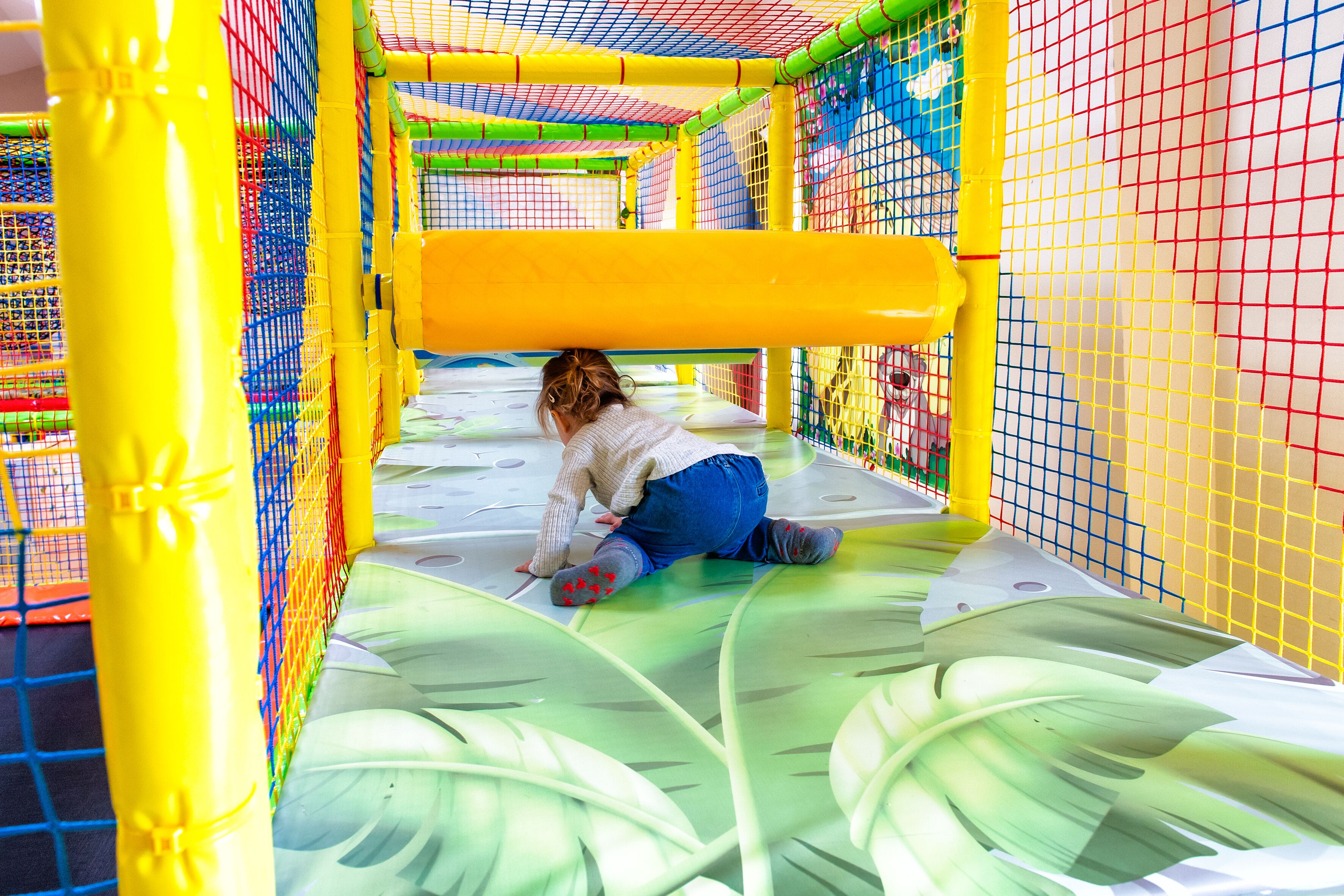 Niño jugando en un área de juegos interior colorida, con paredes de red y superficie acolchada.