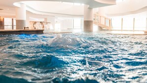 Una piscina interior con un diseño arquitectónico moderno, que destaca por una fuente central y un espacio amplio.
