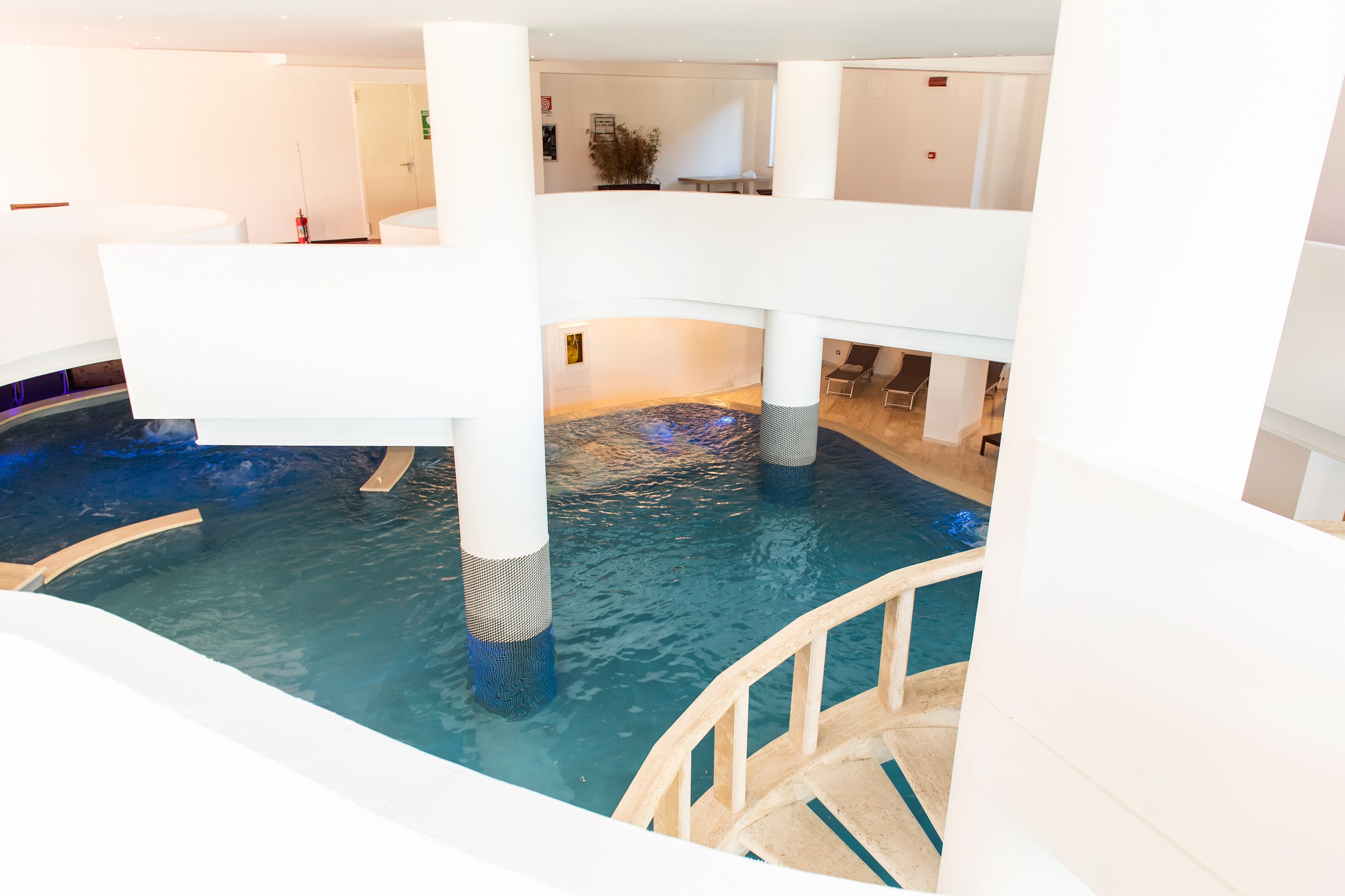 Ein mehrgeschossiges Hallenbad mit klarem Wasser, Holzstufen und weißen Strukturelementen.