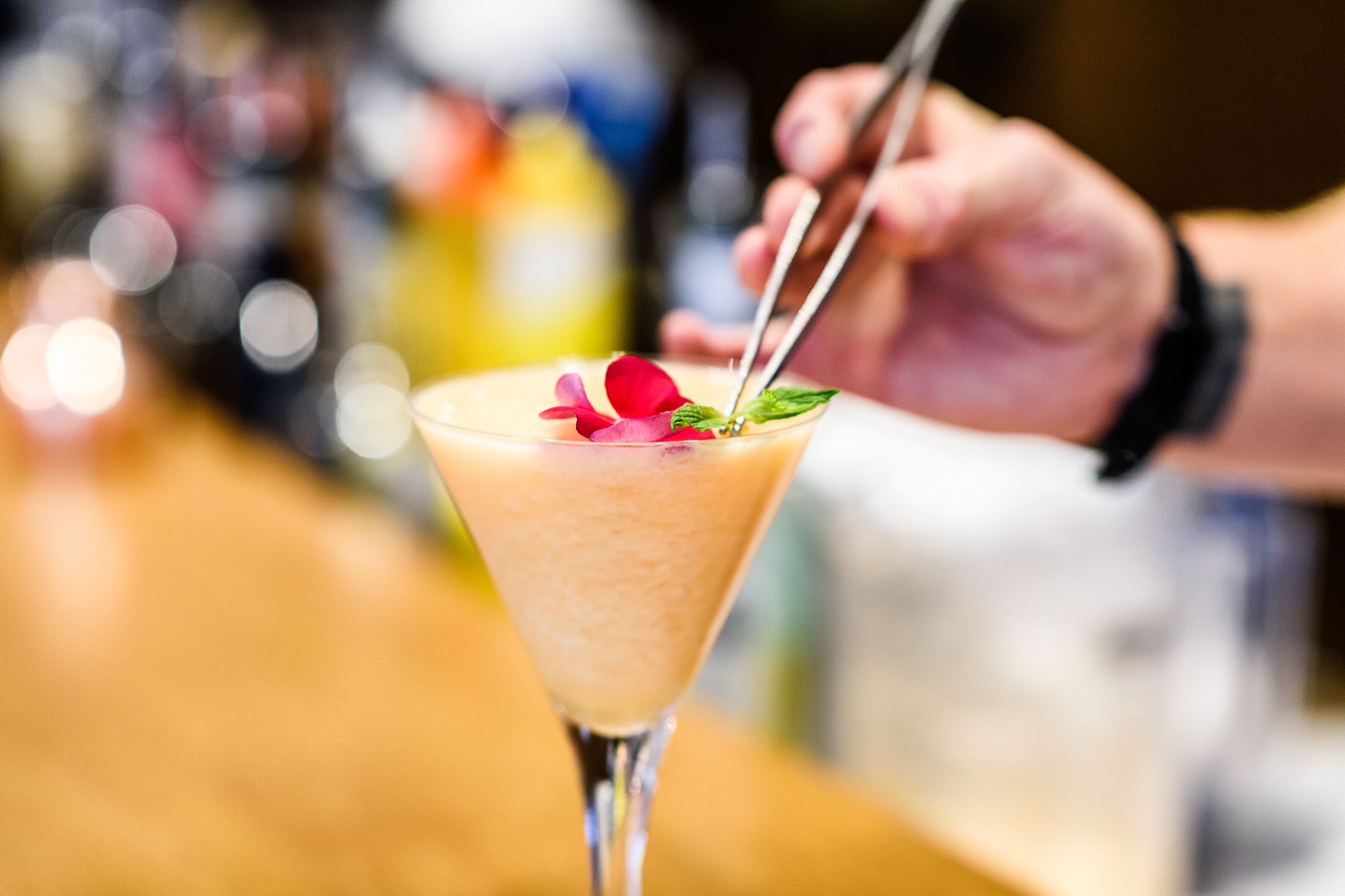A cocktail with a rose garnish and mint leaves, served in a martini glass.