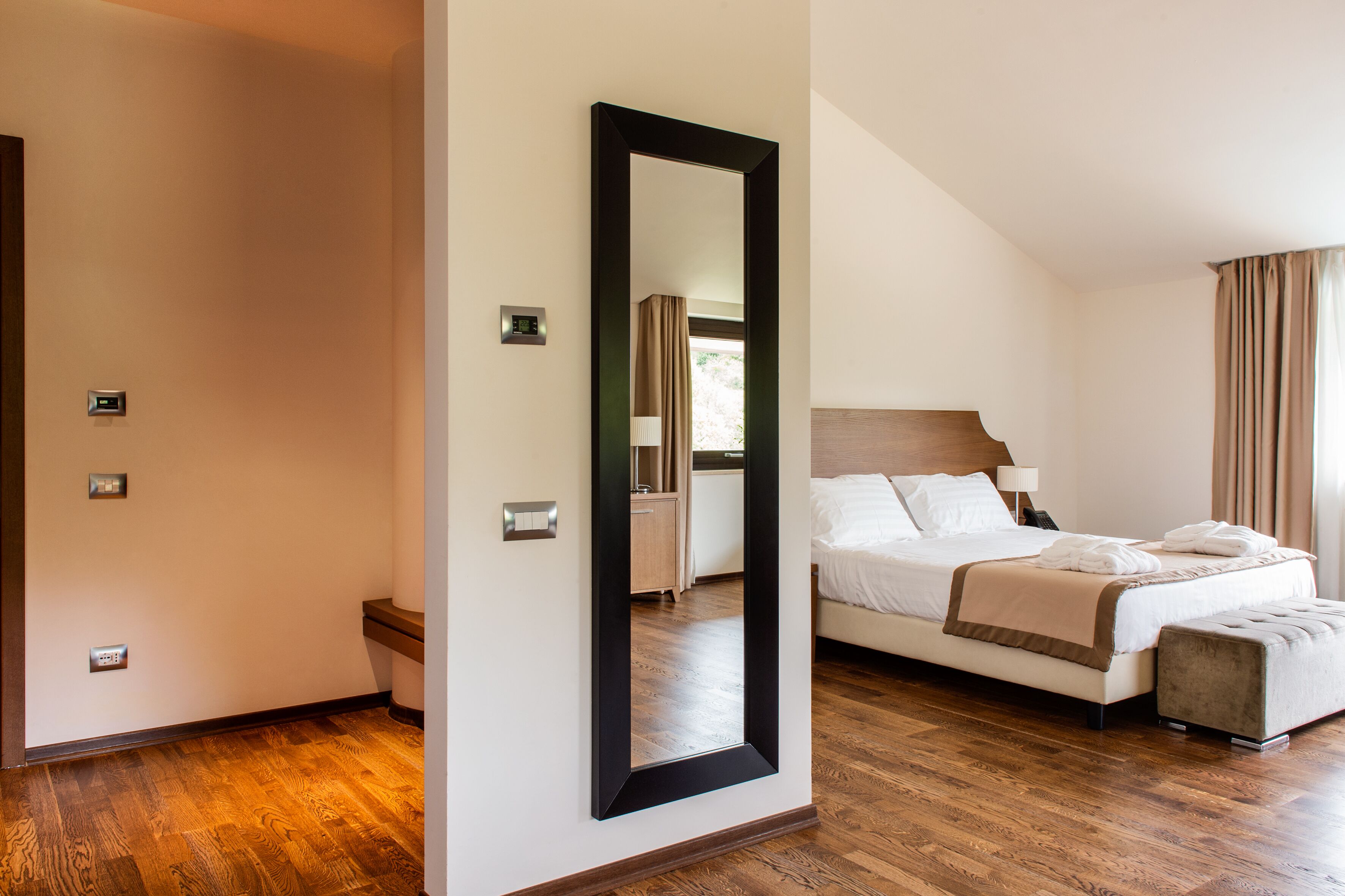 Une chambre d’hôtel avec un grand lit, un plancher en bois, un miroir et une fenêtre avec des rideaux.