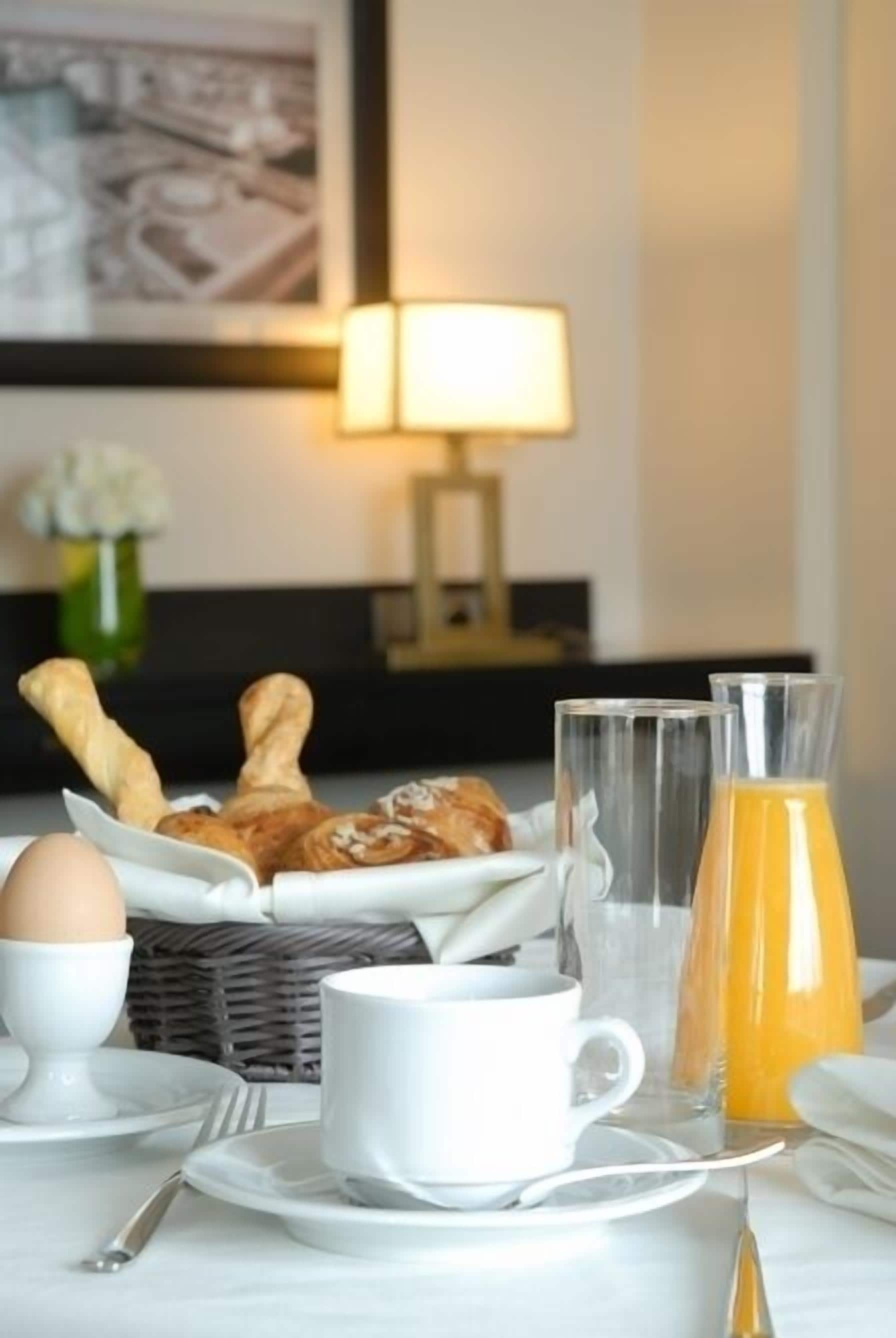 Une table dressée pour le petit-déjeuner avec des croissants, une tasse de café, un verre de jus d’orange et un vase rempli de fleurs.