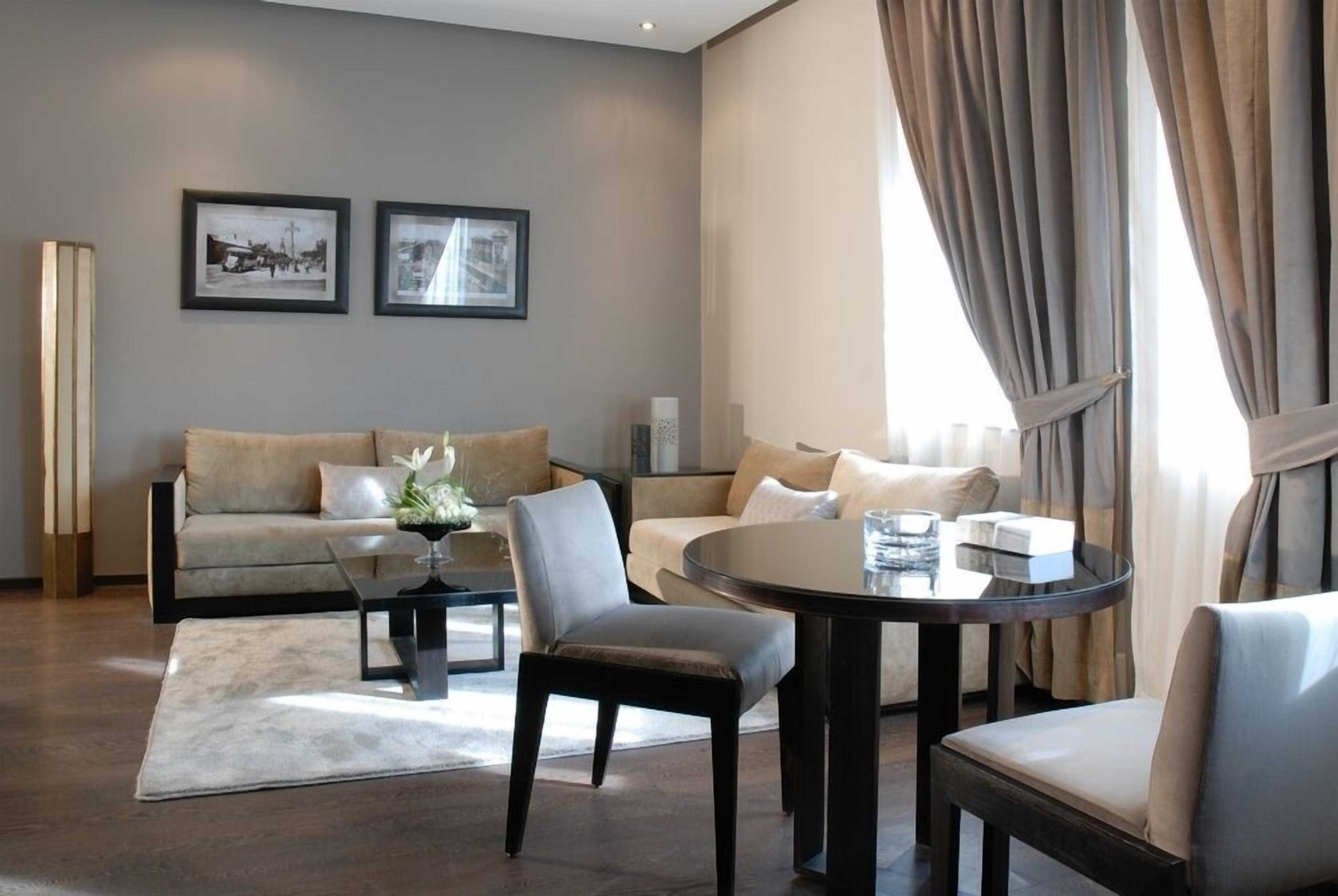 Un salon moderne avec un canapé, des fauteuils, une table basse et une table à manger. Deux tableaux encadrés ornent le mur, et une lampe sur pied est placée dans un coin.