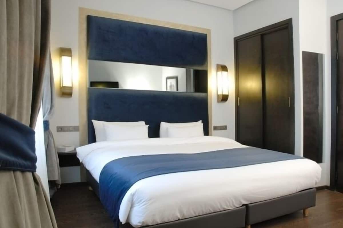 Una habitación de hotel moderna con una cama grande, un cabecero oscuro y dos lámparas de pared.