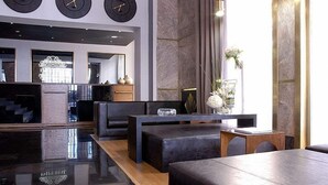 Un hall d’entrée moderne avec des sièges en cuir noir, un comptoir d’accueil et trois horloges fixées au mur.