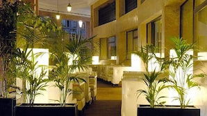 Un hall d’hôtel doté de plusieurs espaces aménagés avec des sièges, des plantes en pot et d’un escalier menant aux étages supérieurs.