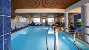 An indoor swimming pool with wooden ceiling beams, tiled walls, and a view of a building outside. - Czarny Potok Wellness & Spa Zakopane Centrum (Zakopane)