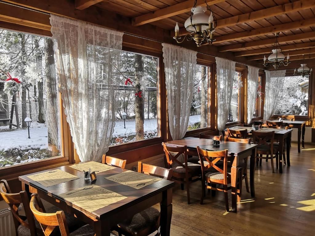 Un restaurante con mesas y sillas de madera, amplias ventanas con cortinas y vistas a un área exterior nevada.