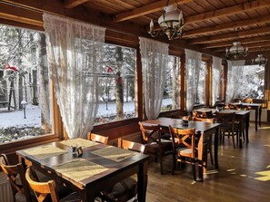 A restaurant with wooden tables and chairs, large windows with curtains, and a view of a snowy outdoor area. - Czarny Potok Wellness & Spa Zakopane Centrum (Zakopane)
