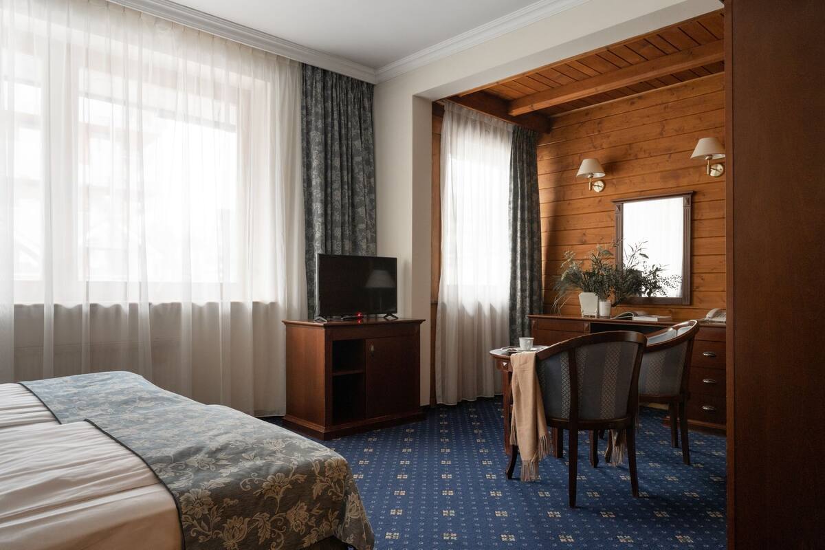 Ett hotellrum med en säng, ett skrivbord med en stol, en tv och ett fönster med gardiner.