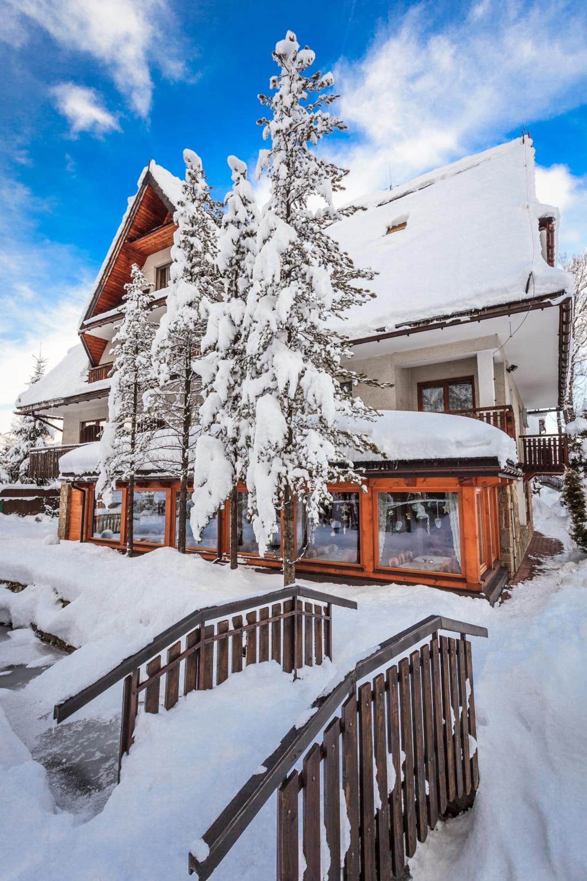 Un chalet enneigé, avec un escalier en bois menant à l’entrée.