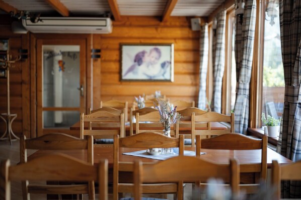 A dining area with wooden tables and chairs, a vase with flowers on one table, and a painting on the wall. - Hotel Belvedere Resort & SPA (Zakopane)