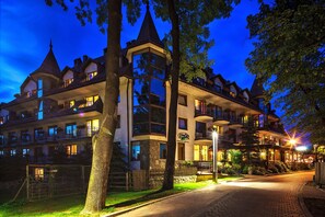 Un hotel de varios pisos con balcones, fachada de piedra y una entrada bien iluminada.