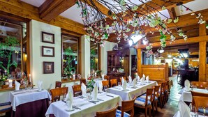 A restaurant with wooden interiors, tables set with white tablecloths and chairs, and hanging floral decorations. - Hotel Litwor (Zakopane)