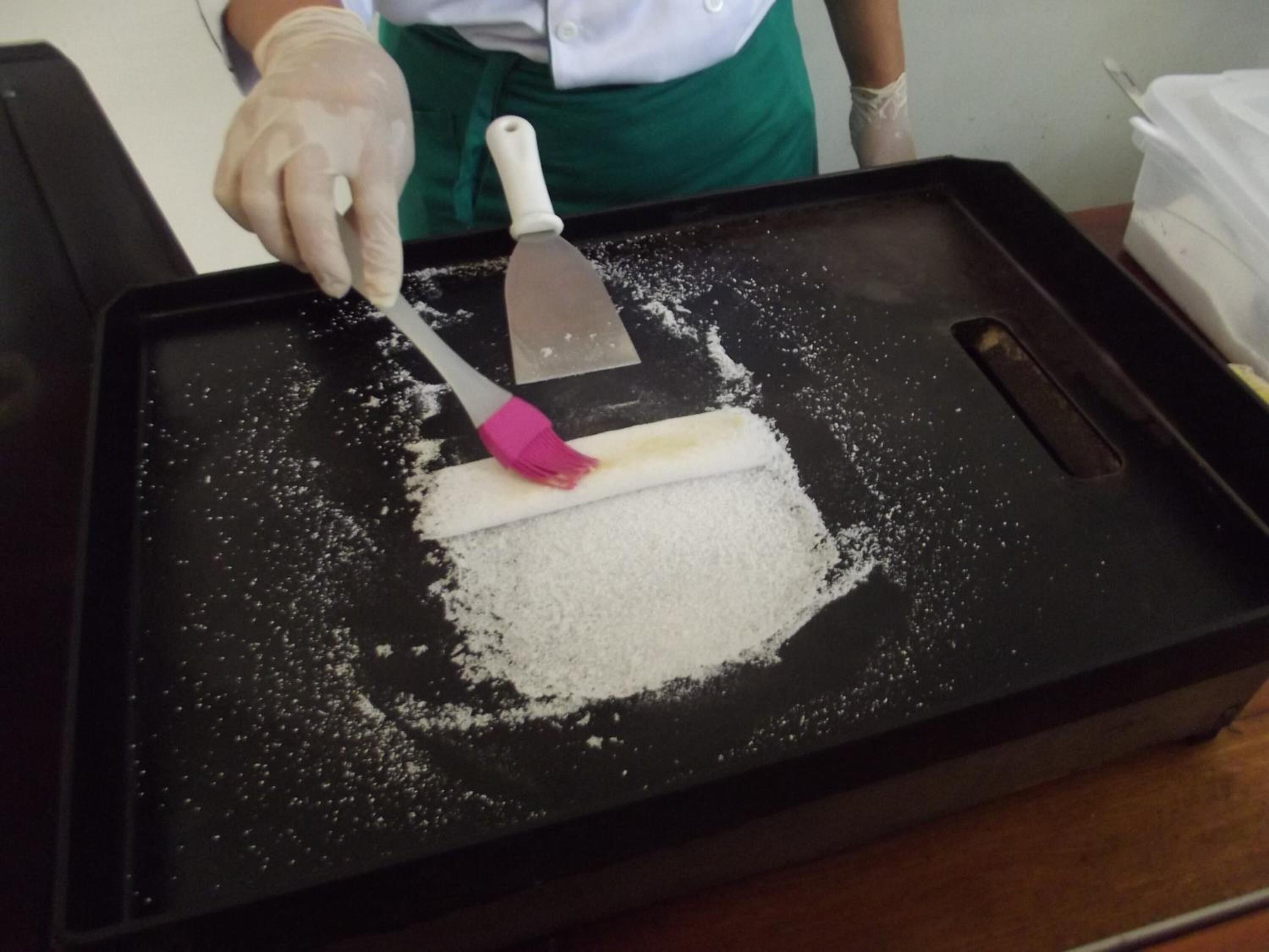 A person using a spatula to spread a white powder on a black tray.