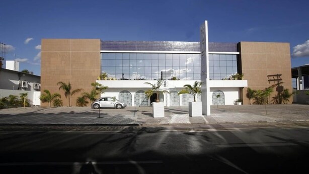 A modern building with a glass facade, palm trees, and a white car parked in front.