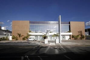 A modern building with a glass facade, palm trees, and a white car parked in front.