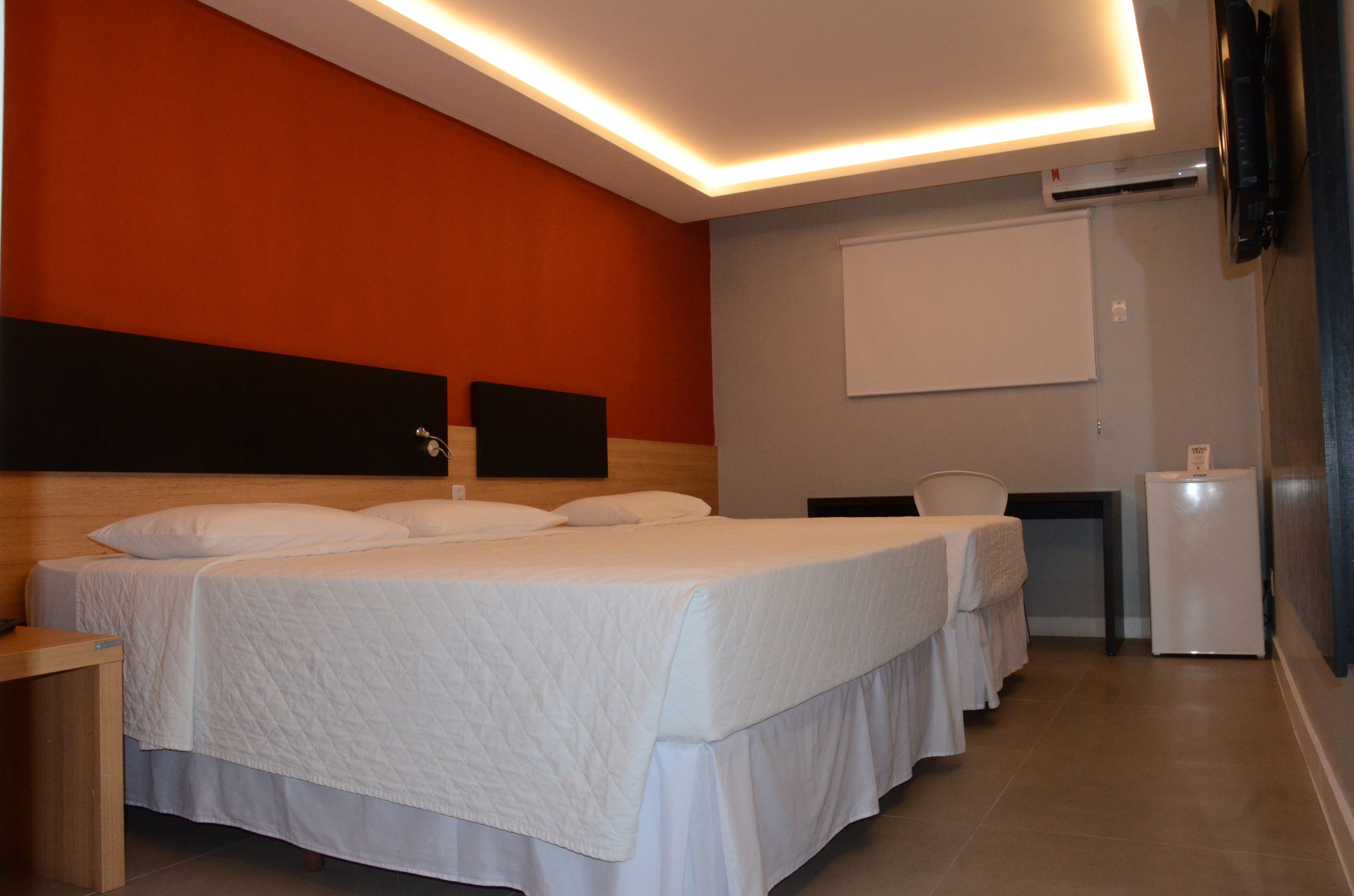 A hotel room with two beds, a desk, a chair, and a small refrigerator.