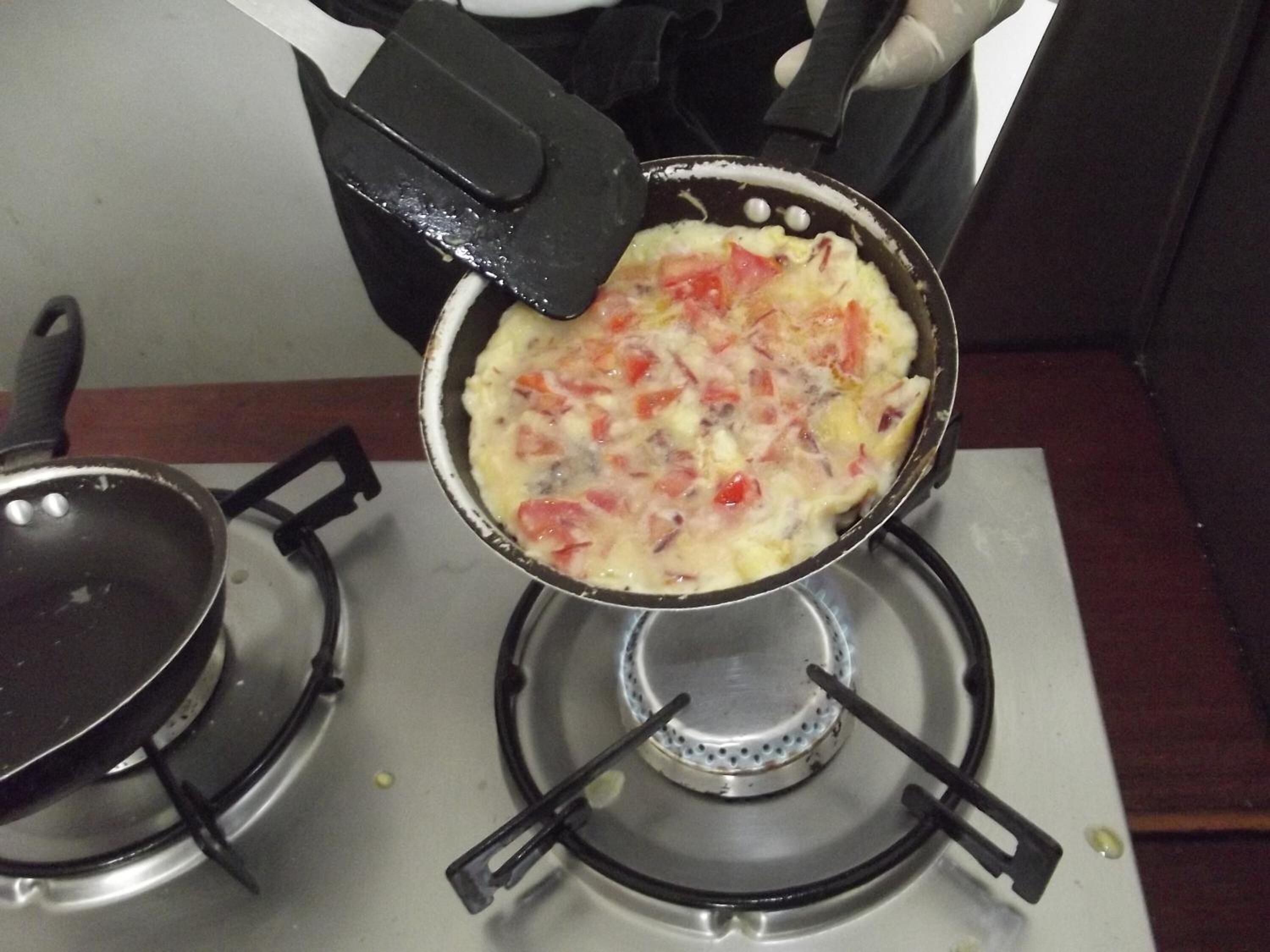 A cooking pan on a stove with a spatula.