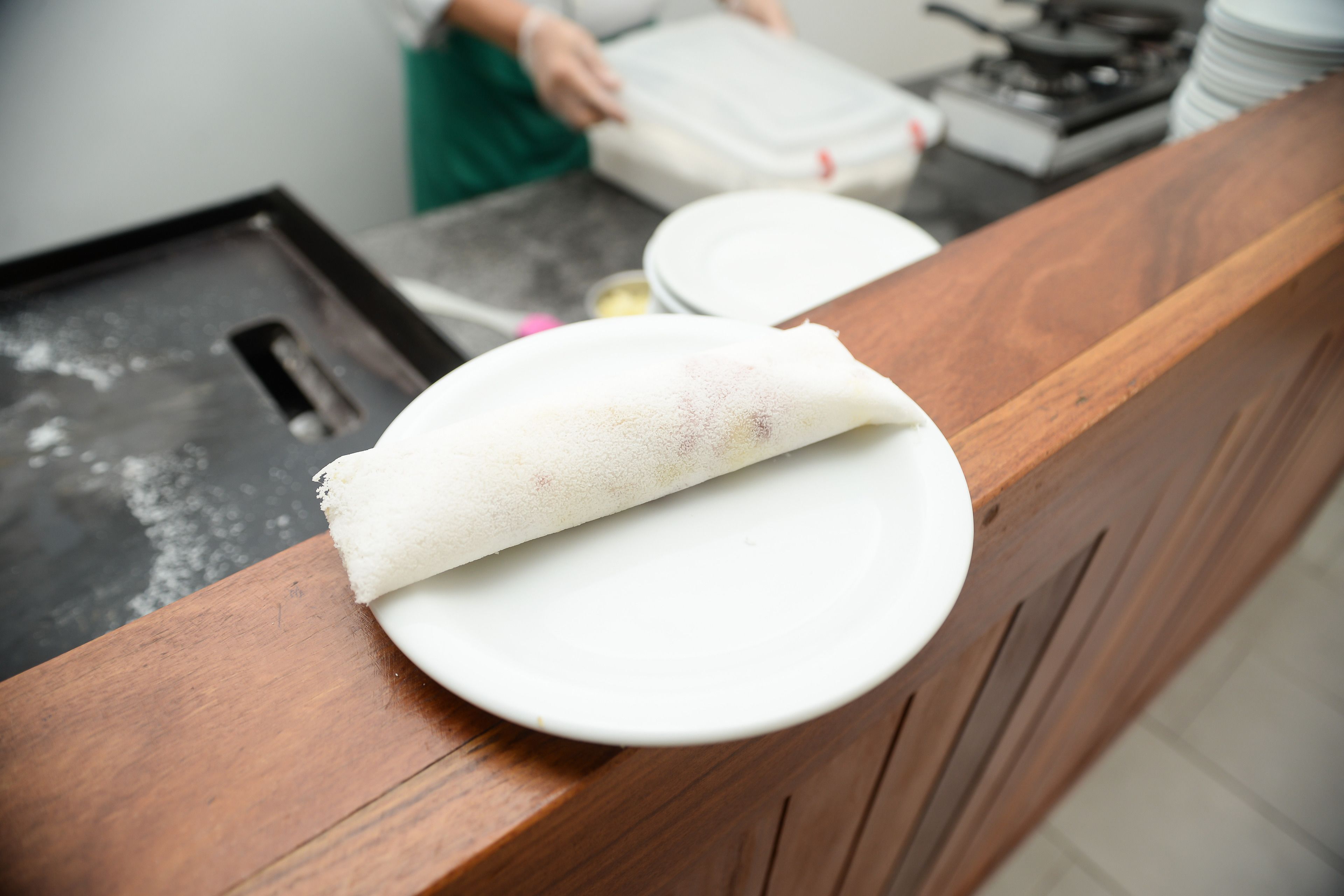 A wooden counter with a white plate and a rolled-up item on it.
