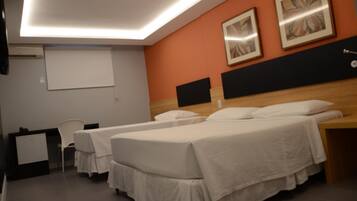 A hotel room with two single beds, a desk, a chair, and a projector screen.