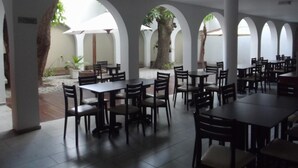 A spacious outdoor dining area with multiple tables and chairs, surrounded by white columns and arches.