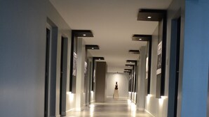 A long, narrow hallway with a polished floor, recessed lighting, and a person walking towards the end.
