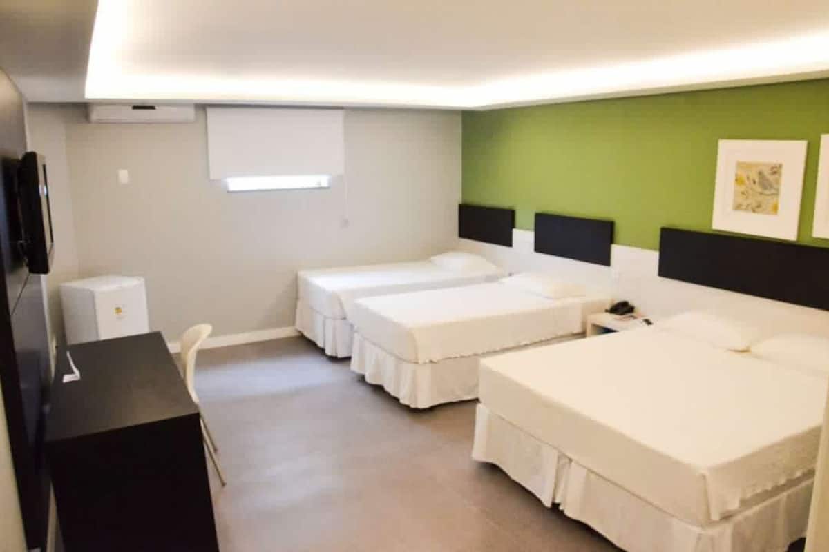 Quarto de hotel com duas camas de solteiro, uma escrivaninha, uma cadeira e uma mesa pequena.
