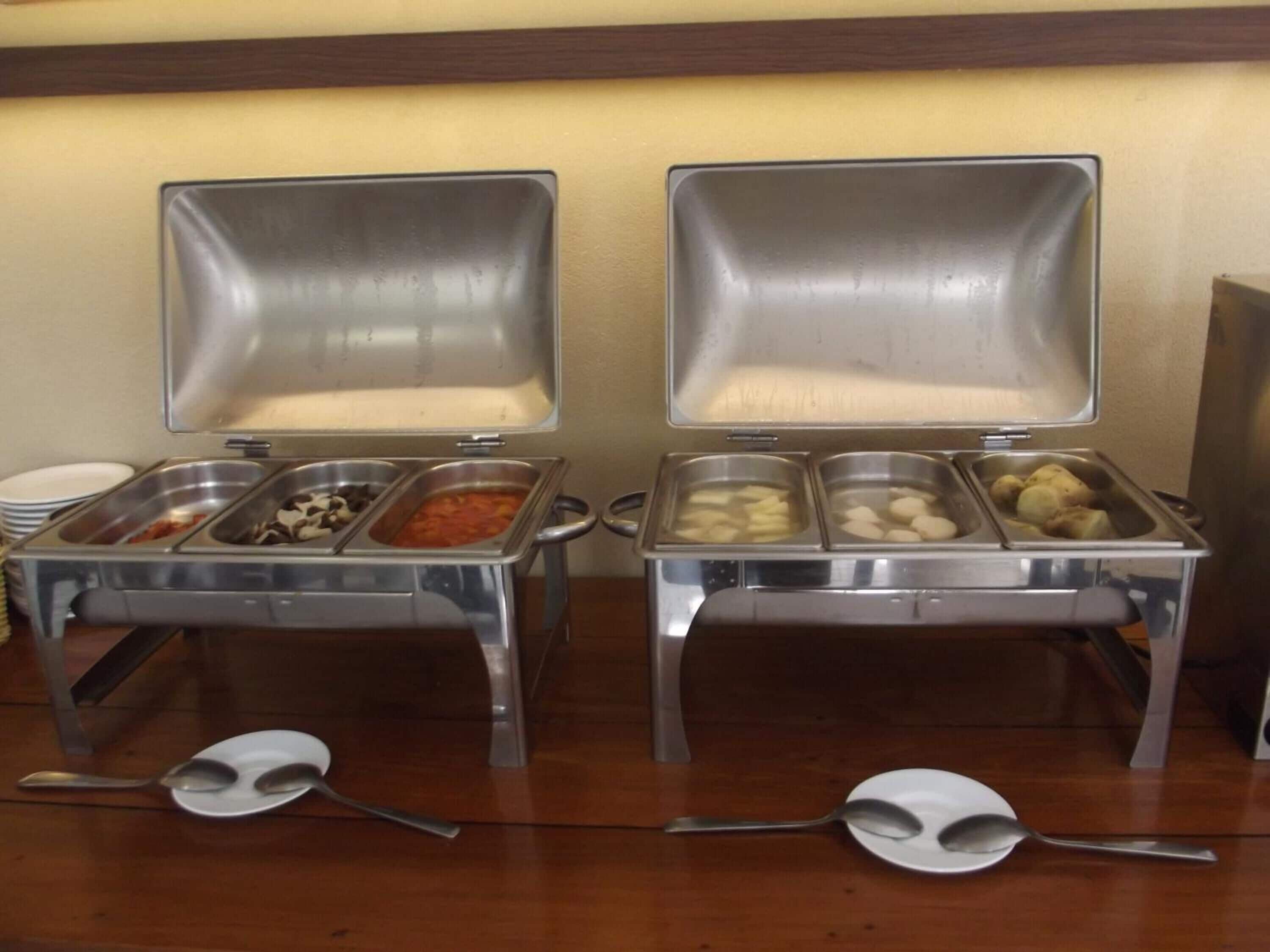Dos estaciones de buffet con diversos alimentos y utensilios de servicio.