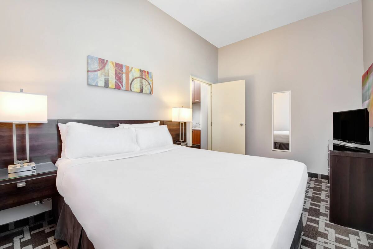 Une chambre d’hôtel avec un grand lit, des tables de chevet, une télévision, un miroir et un tableau au mur.