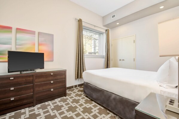 A hotel room with a bed, a TV on a dresser, a window with curtains, and a painting on the wall. - Willowdale Hotel Toronto North York (Toronto)