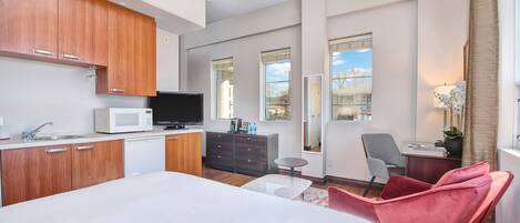 A modern hotel room with a kitchen area, a large bed, a desk, and a chair.