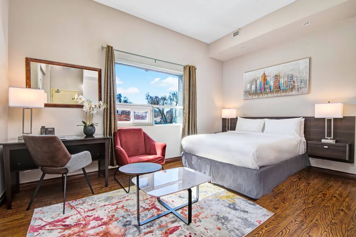Une chambre d’hôtel équipée d’un lit, d’un bureau, d’une chaise et offrant une vue sur le paysage urbain à travers la fenêtre.