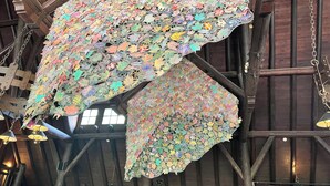 A large, intricate chandelier made of colorful paper leaves suspended in a high-ceilinged room with wooden beams. - Pere Marquette Lodge & Conference Ctr. (Grafton)