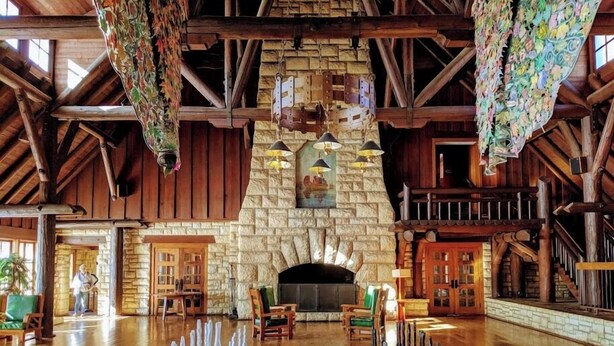 A spacious lobby with a large checkered floor game, a stone fireplace, and wooden beams. - Pere Marquette Lodge & Conference Ctr. (Grafton)